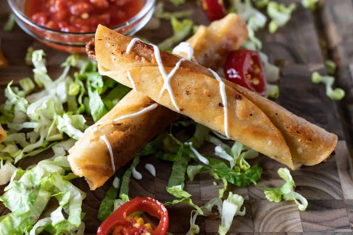 Two crispy spring rolls on a bed of lettuce with sliced red chilies and a bowl of dipping sauce, served on a wooden surface.