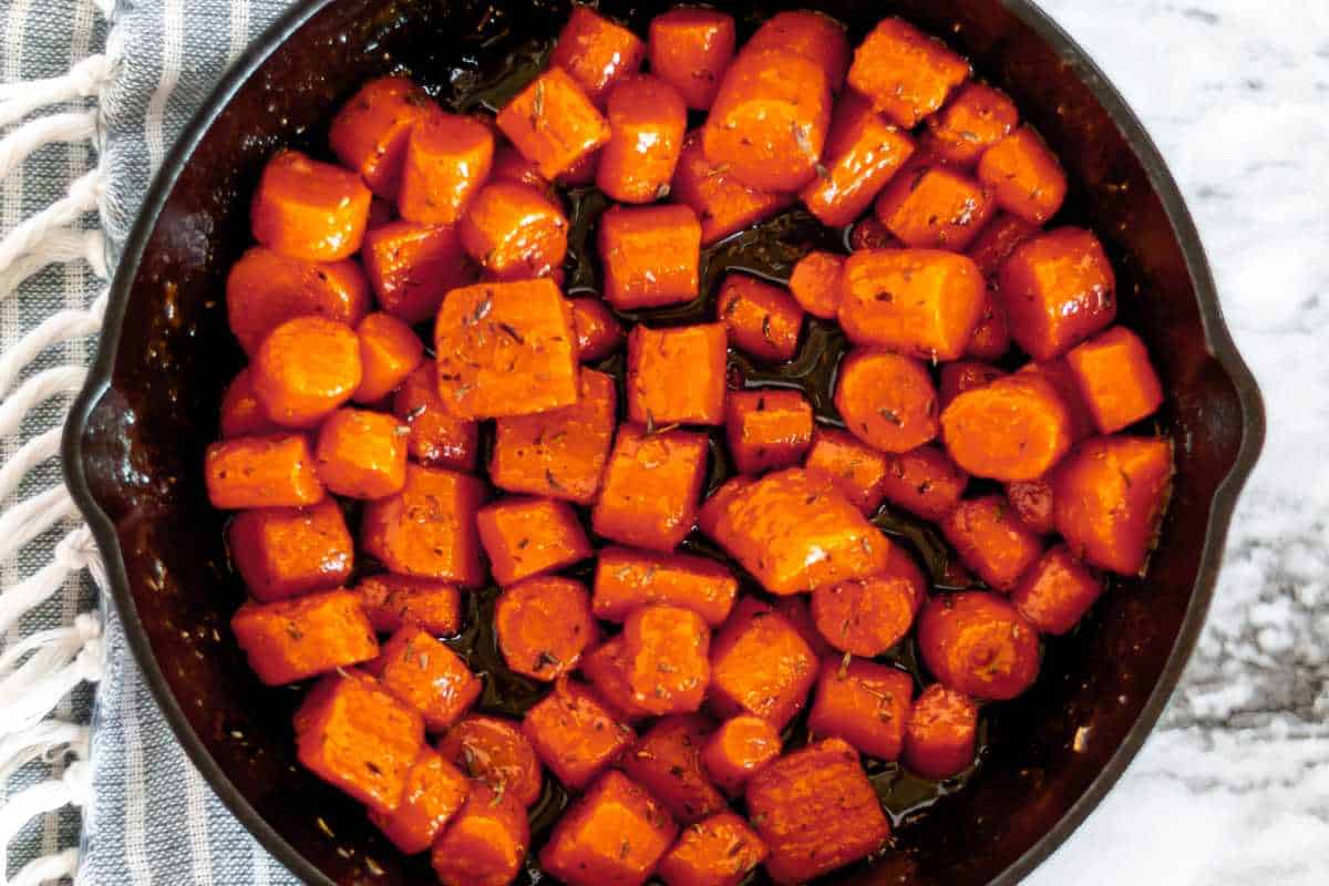 Roasted sweet potato cubes in a cast iron skillet on a marble countertop with a striped cloth nearby.