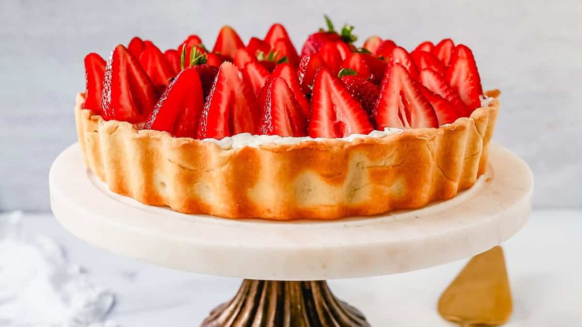 A strawberry tart on a white pedestal with a gold cake server on the side.