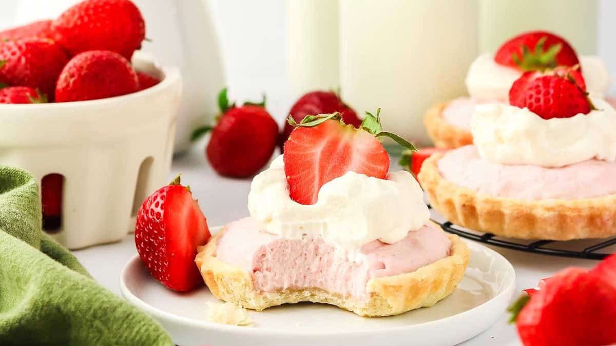 A strawberry tart topped with whipped cream, alongside fresh strawberries and glasses of milk.