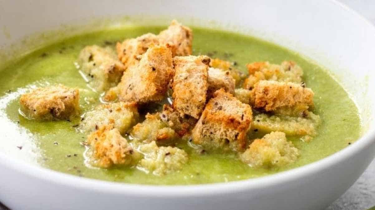 A bowl of creamy green vegetable soup topped with golden-brown croutons.