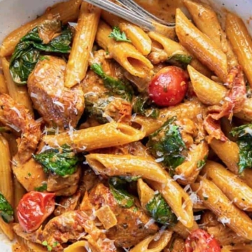 Creamy tomato pasta with spinach and chicken in a white bowl.