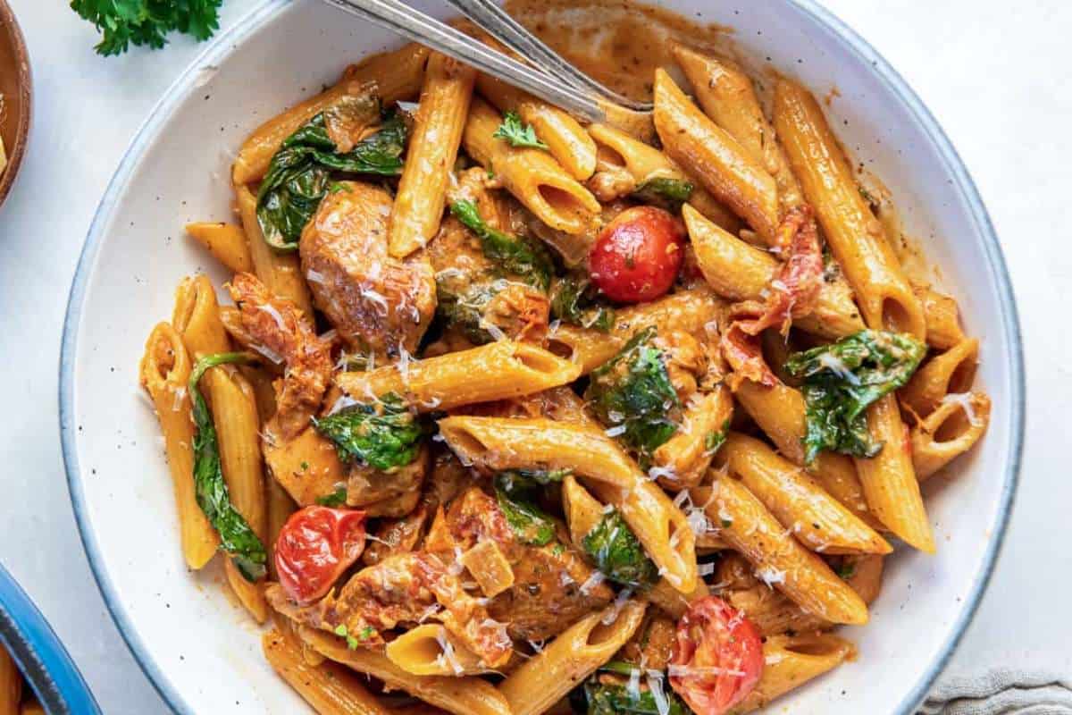 Creamy tomato pasta with spinach and chicken in a white bowl.