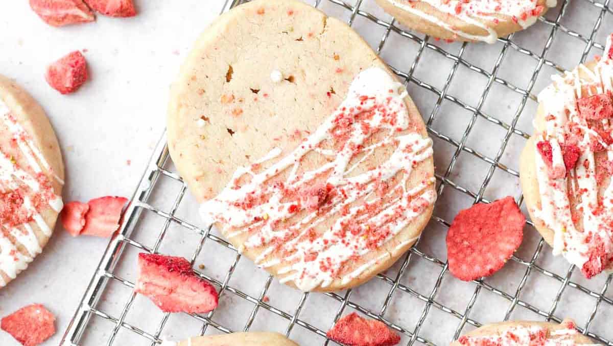 Cookies with white frosting and pink sprinkles on a cooling rack.