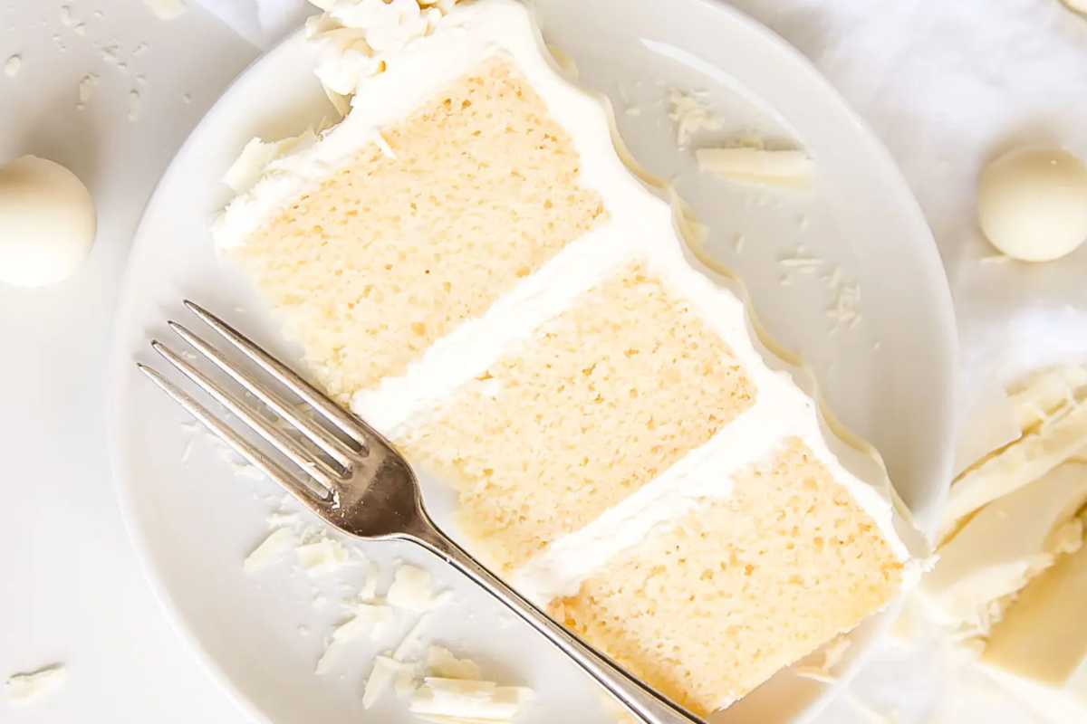 Two slices of white coconut cake on a plate with a fork, surrounded by shredded coconut pieces.