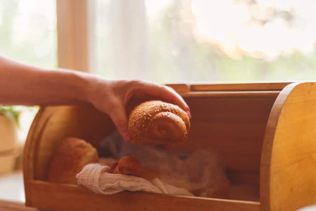 woman taking a bread loaf from a bread box in the kitchen at home