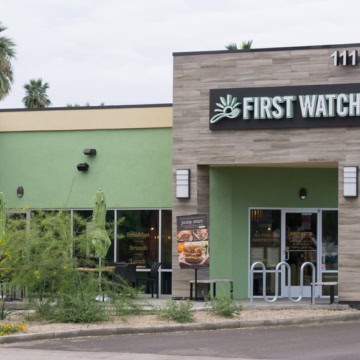 A First Watch restaurant exterior, featuring modern architecture with green and gray walls, and labeled with signage.