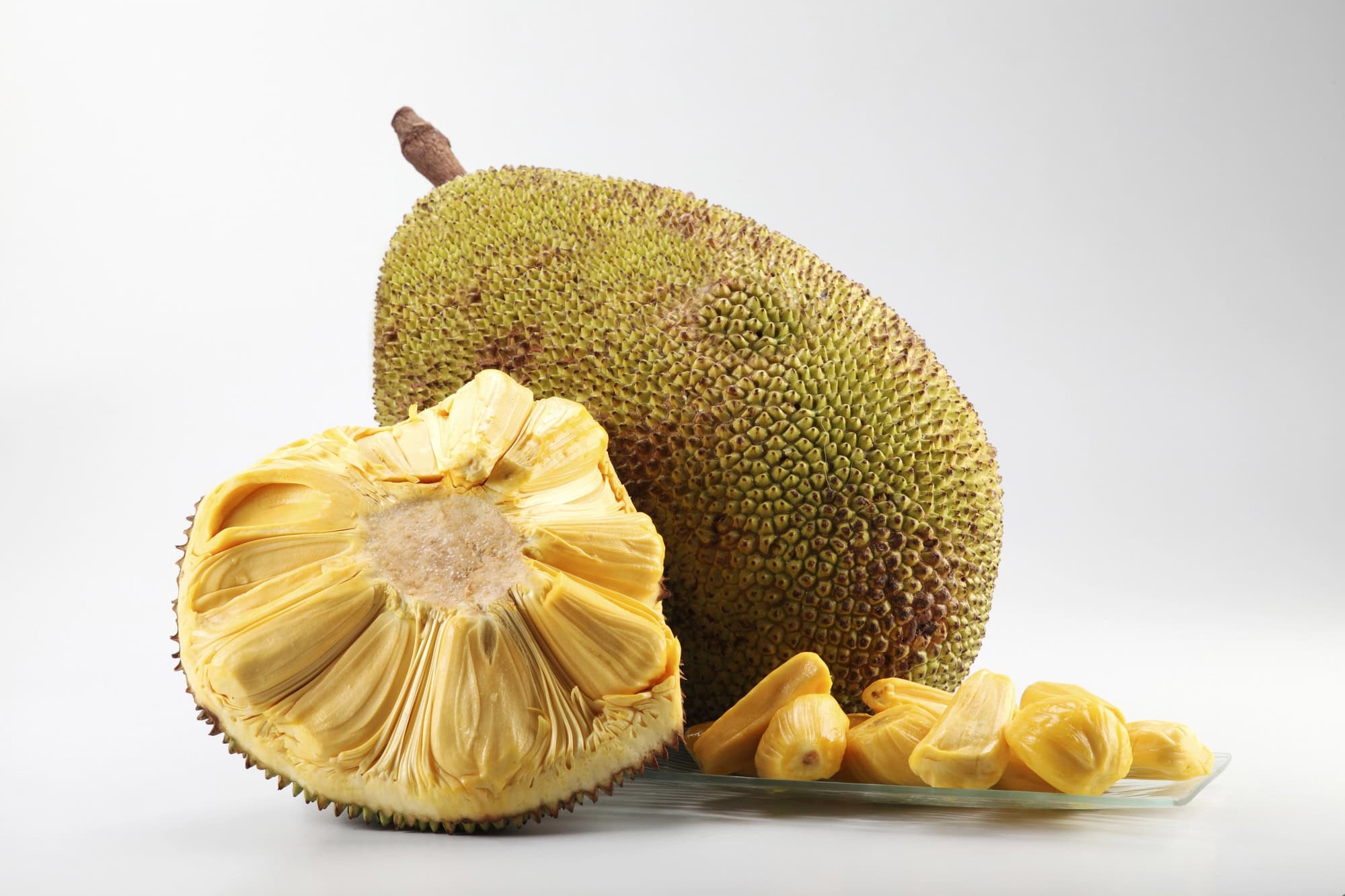 Whole and sliced jackfruit with visible seeds on a light background.