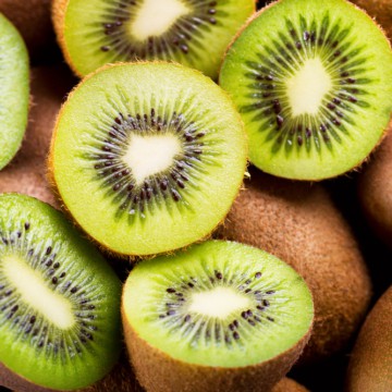 Sliced kiwi fruits displaying vibrant green flesh with black seeds, arranged among whole, brown, fuzzy kiwi skins.