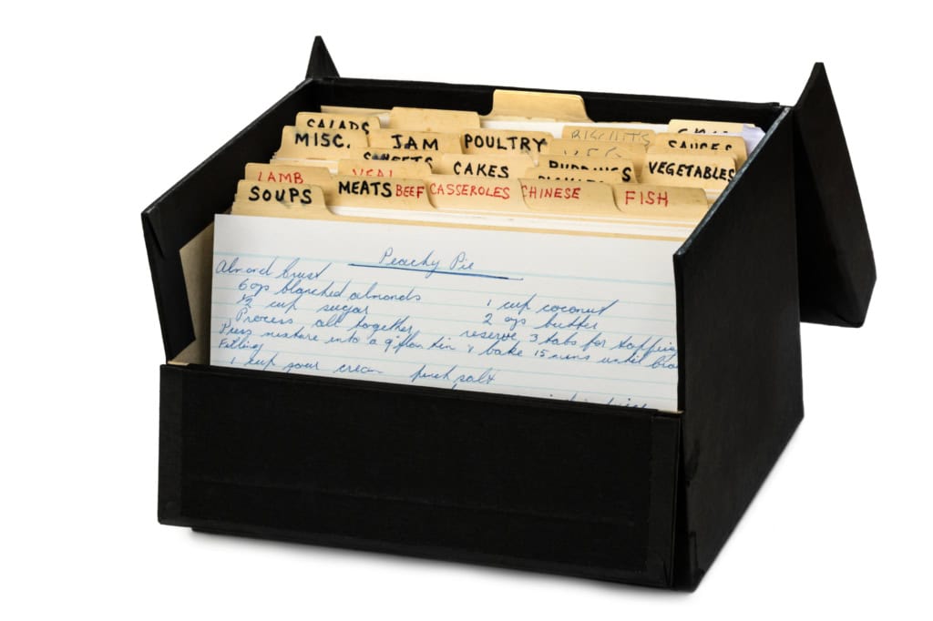 A black recipe box filled with categorized and handwritten recipe cards, labels visible include "cakes," "fish," and "chinese.