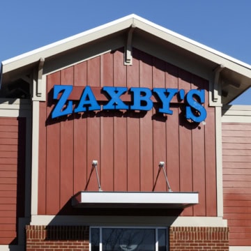 The front of a Zaxby's restaurant with a blue sign on a red wooden exterior under a clear blue sky invites guests to explore favorites like the zaxby's gluten free menu.