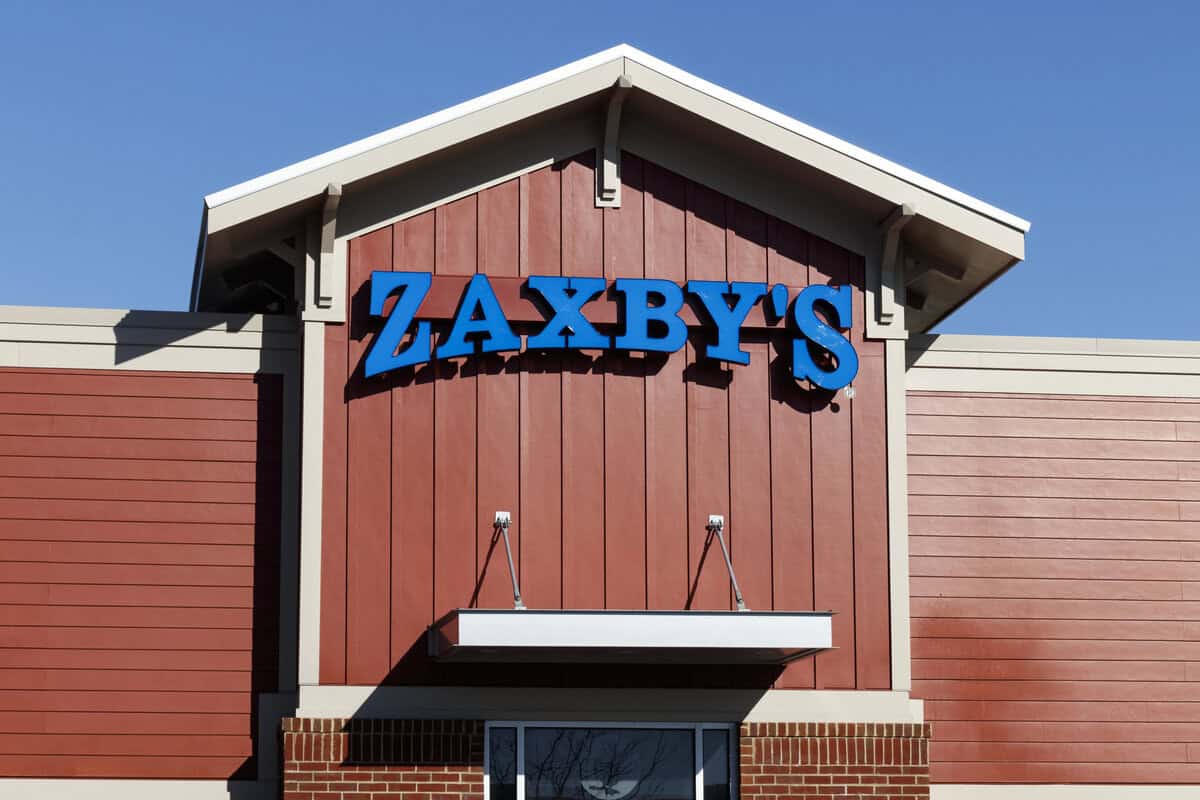 The front of a Zaxby’s restaurant with a blue sign on a red wooden exterior under a clear blue sky invites guests to explore favorites like the zaxby’s gluten free menu.