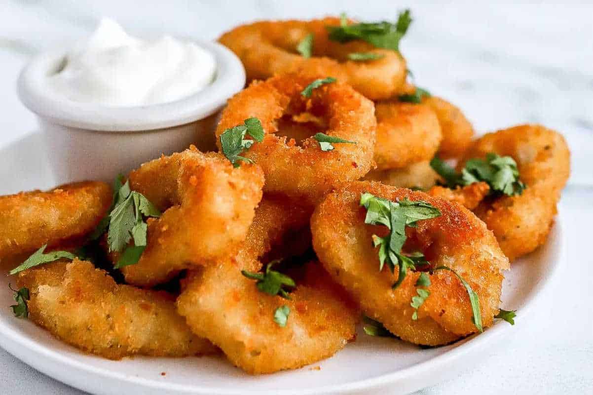 A plate of golden-fried shrimp garnished with parsley, accompanied by a small bowl of white dipping sauce.