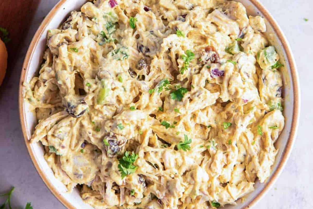 A bowl of creamy chicken salad with celery, raisins, and herbs, viewed from above.