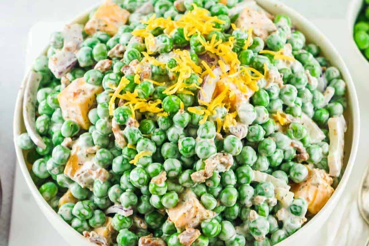 A bowl of pea salad topped with shredded cheddar cheese; the salad includes peas, diced chicken, and a creamy dressing.