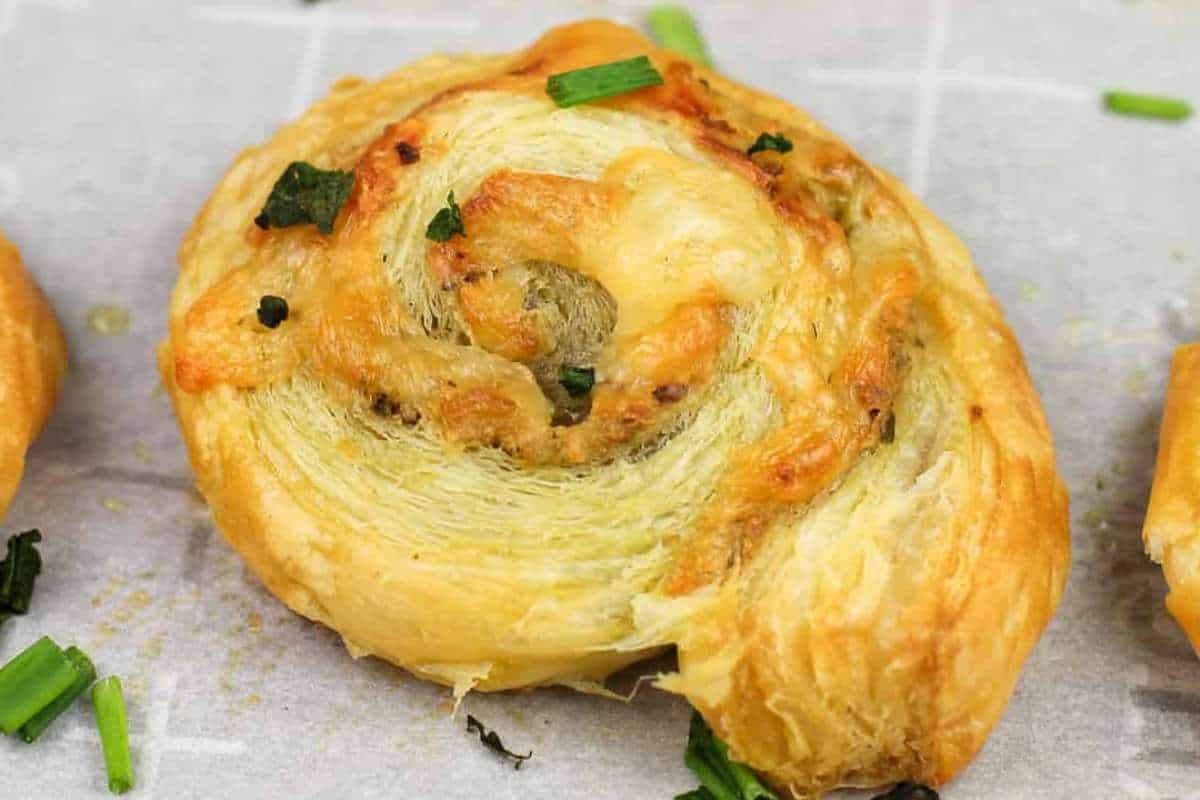A freshly baked, golden pastry pinwheel with melted cheese and chopped green onions on top, sitting on a parchment-lined baking sheet.