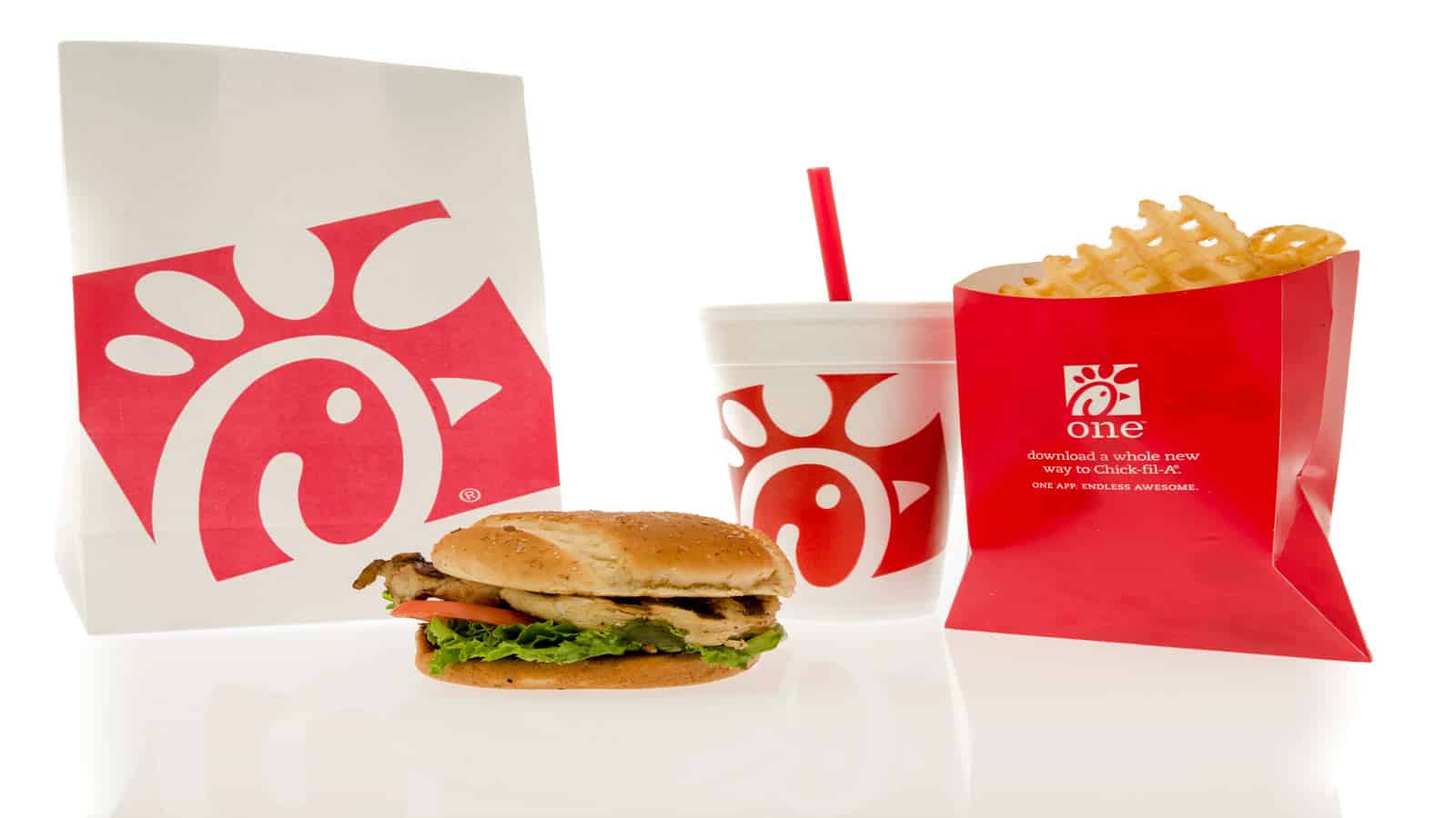 Chick-fil-A meal with a chicken sandwich, waffle fries in a red container, a drink with a red straw, and a branded takeout bag on a white background.