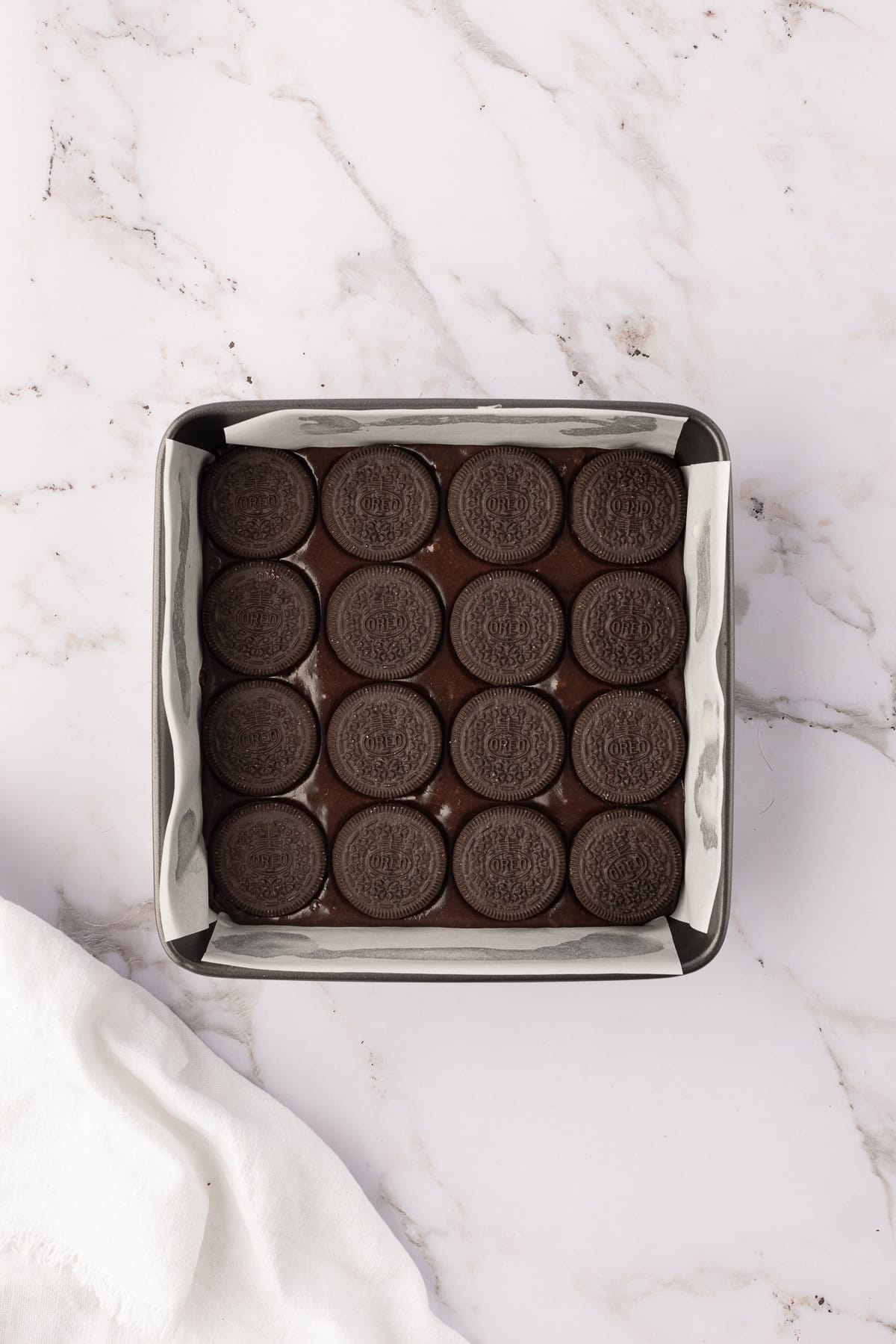 A square baking pan lined with cookies in a grid pattern on a marble surface. A white cloth is partially visible on the side.