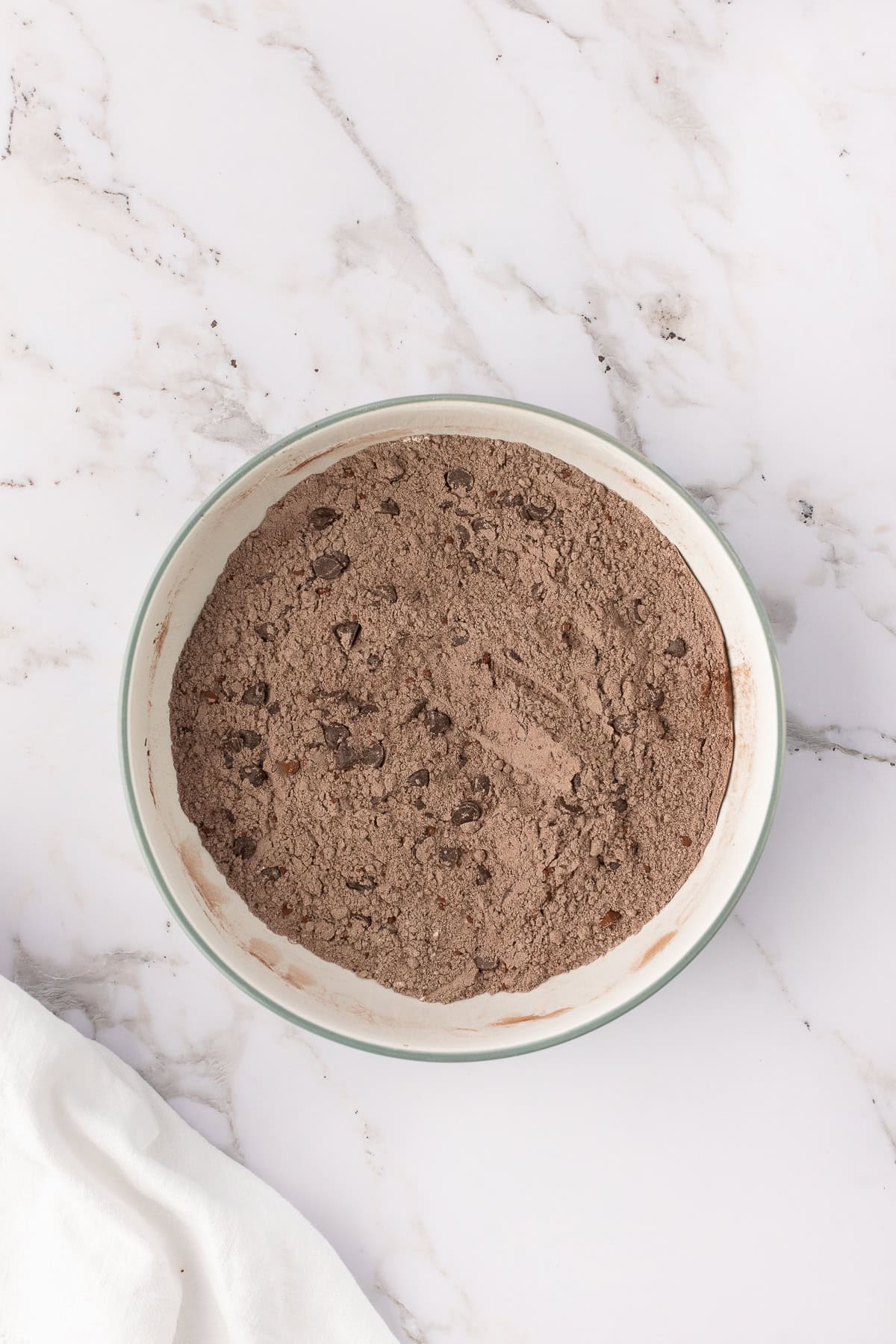 A bowl of dry chocolate cake mix on a marble surface.