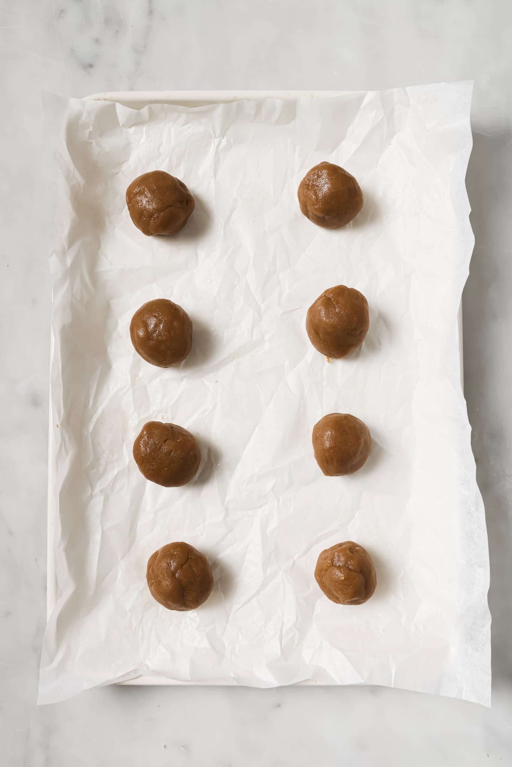 Eight cookie dough balls on a parchment-lined baking sheet.