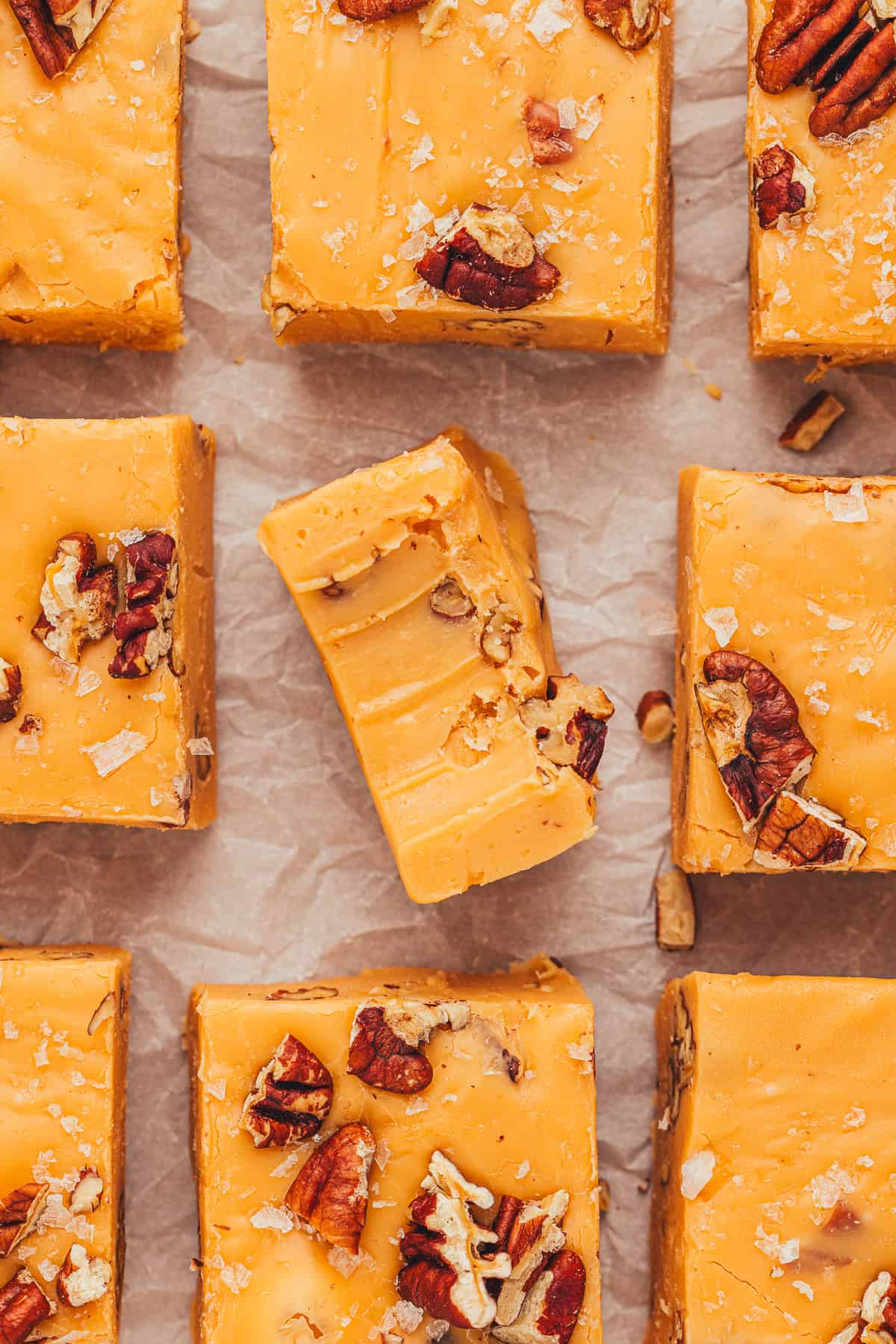 Orange fudge squares with nuts on top, arranged on parchment paper. One piece has a bite taken out.