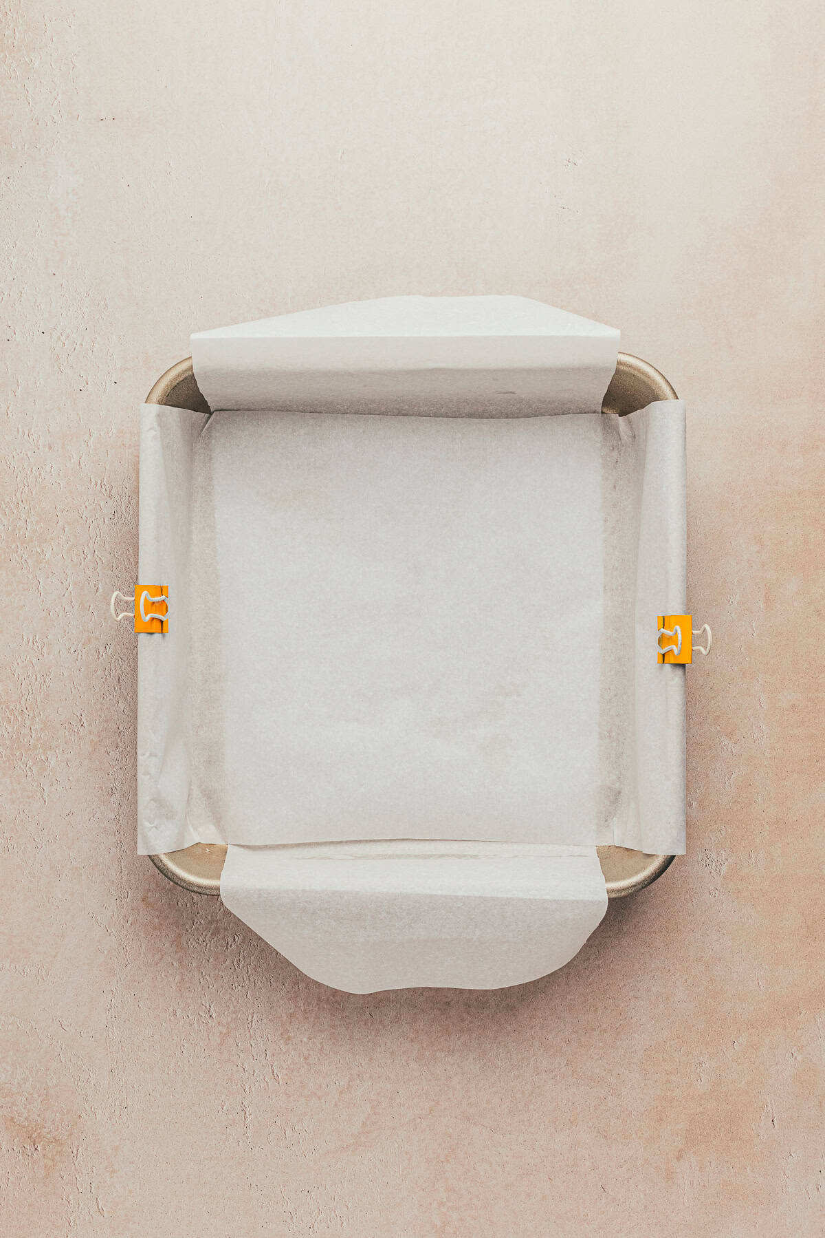 A baking pan lined with parchment paper, secured with two yellow clips on opposite sides.