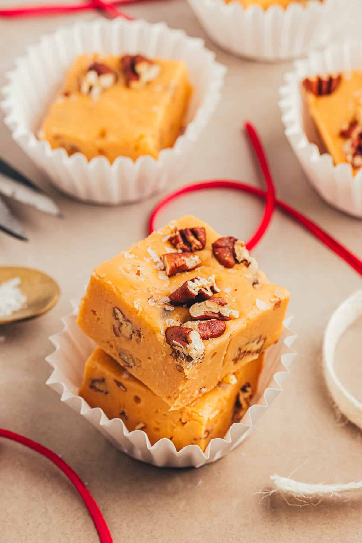 Close-up of two pieces of pecan fudge in a white paper cup, surrounded by red ribbons and more fudge pieces in the background.