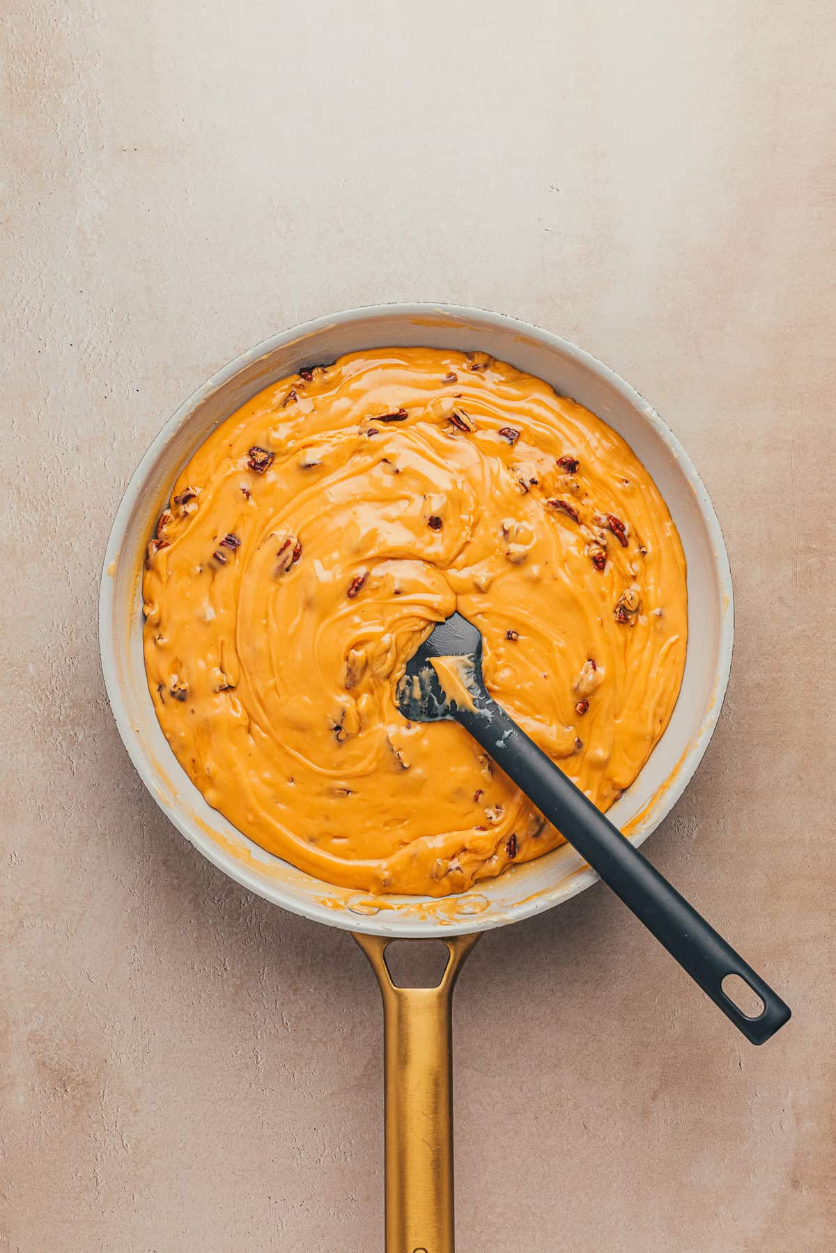 A pan filled with creamy orange cheese sauce mixed with pieces of meat, with a black spatula resting inside.