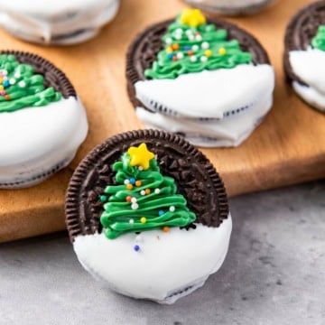 Chocolate cookies decorated with white icing and green frosting shaped like Christmas trees, topped with sprinkles and yellow stars, displayed on a wooden board.