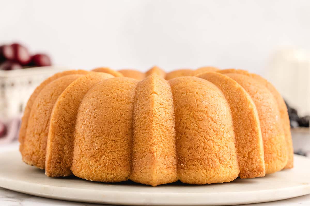 A golden bundt cake on a white plate, with a textured surface and a decorative scalloped design.