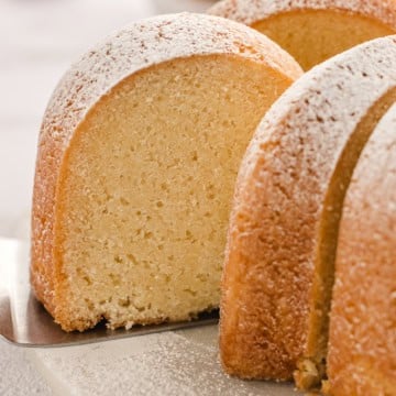 Close-up of a sliced bundt cake topped with powdered sugar on a serving utensil, showing its dense and moist texture.