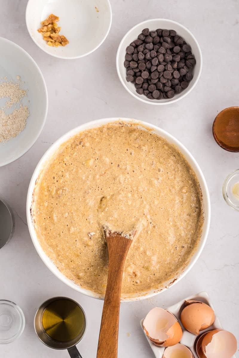 batter for banana muffins in a mixing bowl with wooden spoon
