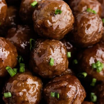 A close-up of glazed meatballs topped with chopped green onions.
