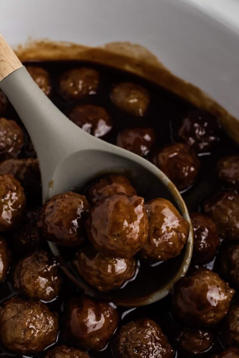 A spoon lifting savory meatballs from a dish filled with dark sauce.