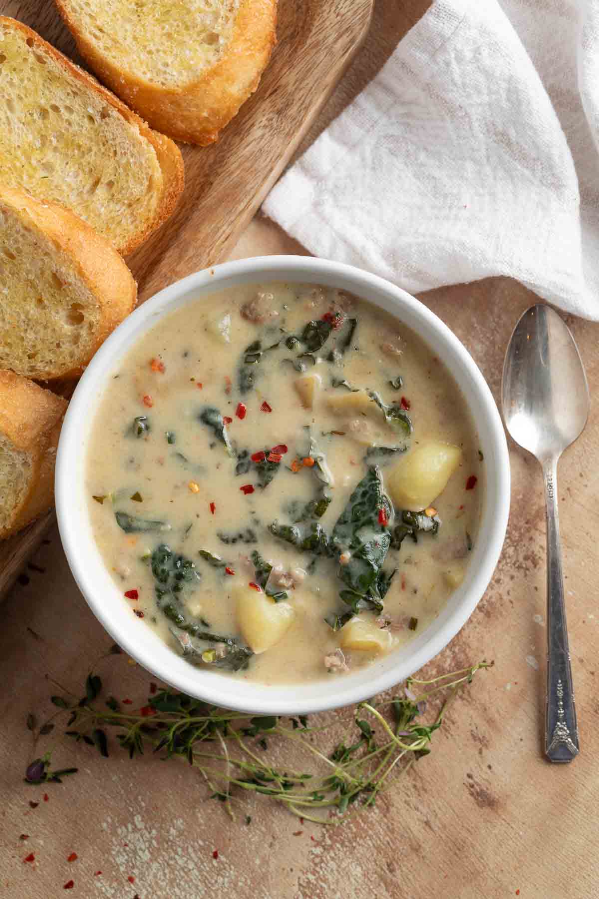 italian sausage soup on a white bowl with crusty bread on the side
