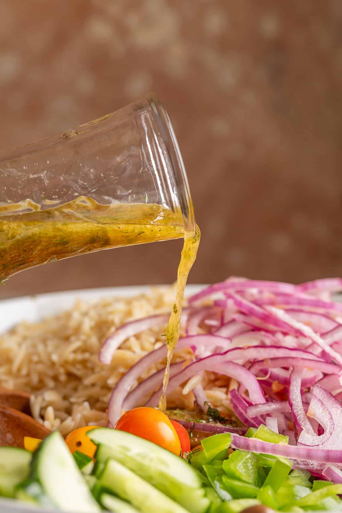 pouring greek dressing over the orzo salad