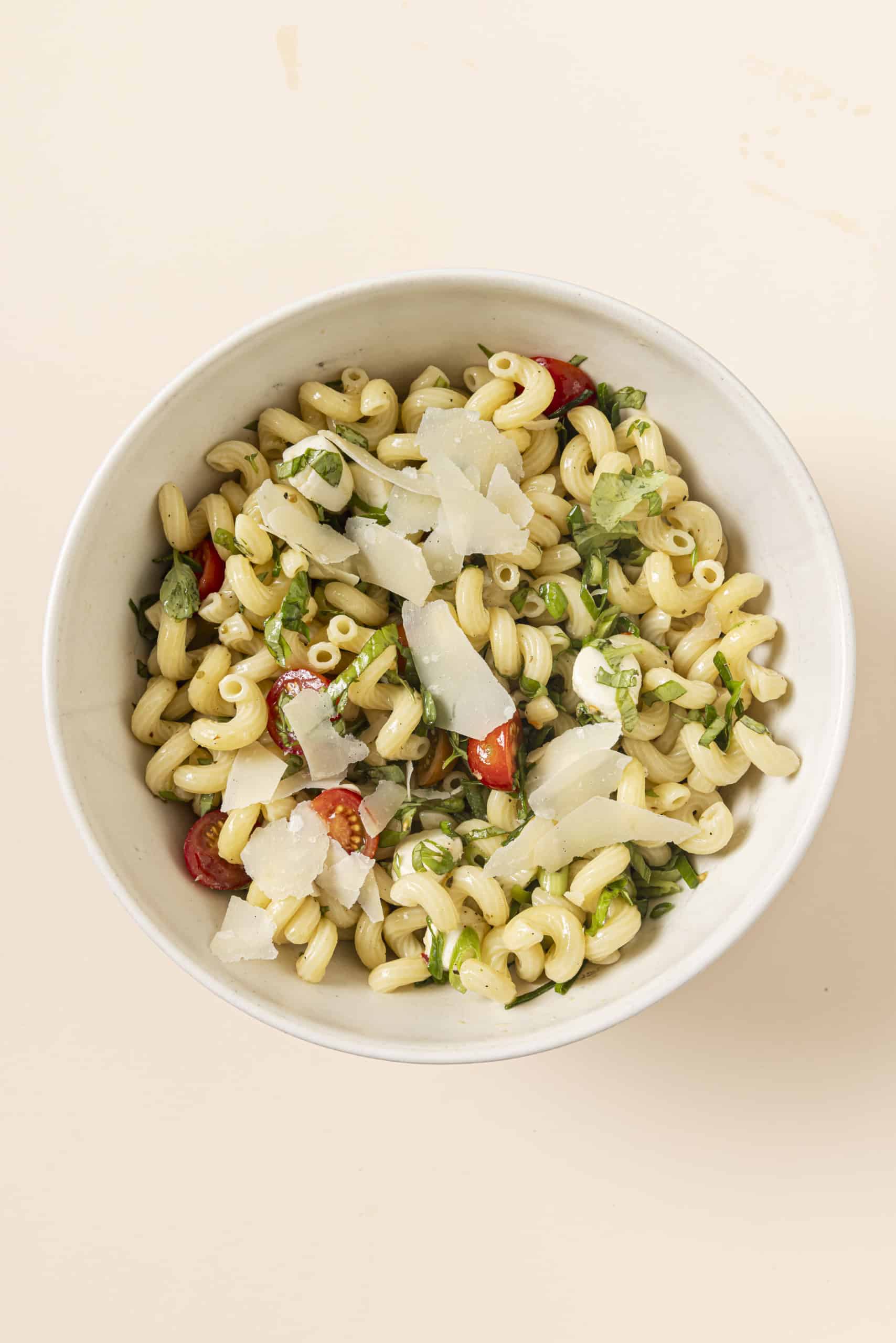 shaved parmesan on top of pasta salad in a bowl