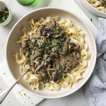 Creamy mushroom beef stroganoff over egg noodles, garnished with fresh herbs, perfect comfort food.