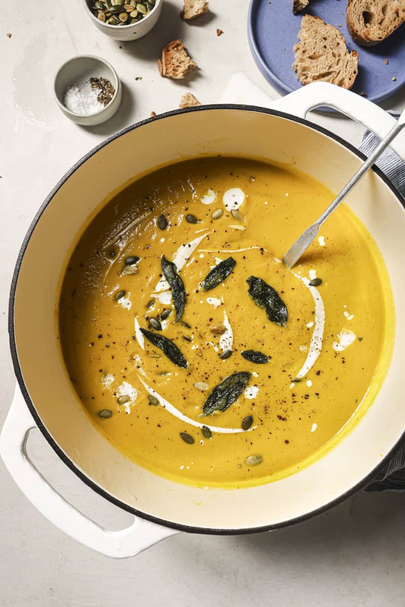 Creamy butternut squash soup with sage and pumpkin seeds in a white pot.