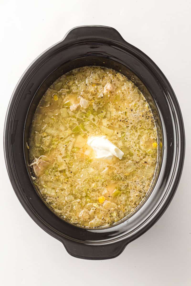 Creamy chicken soup in a black slow cooker with vegetables and herbs.
