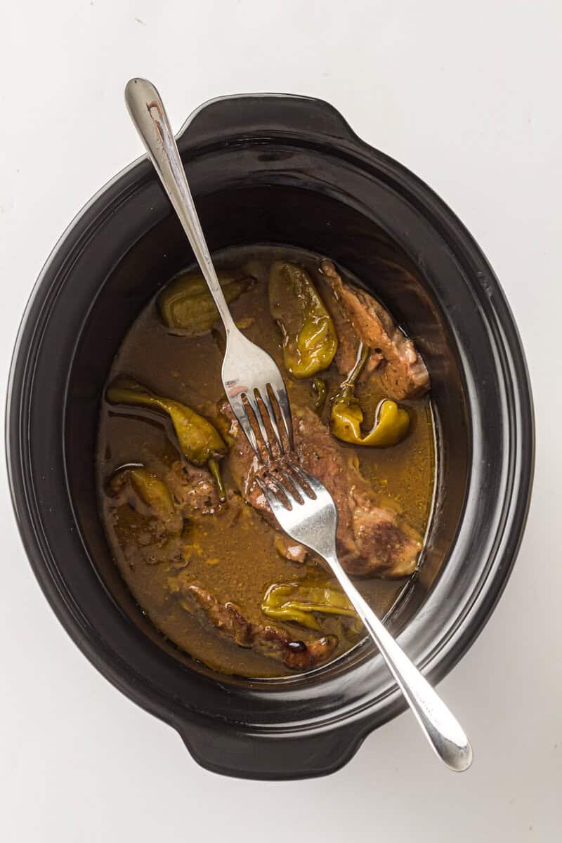 pork roast in slow cooker with two forks shredding pork