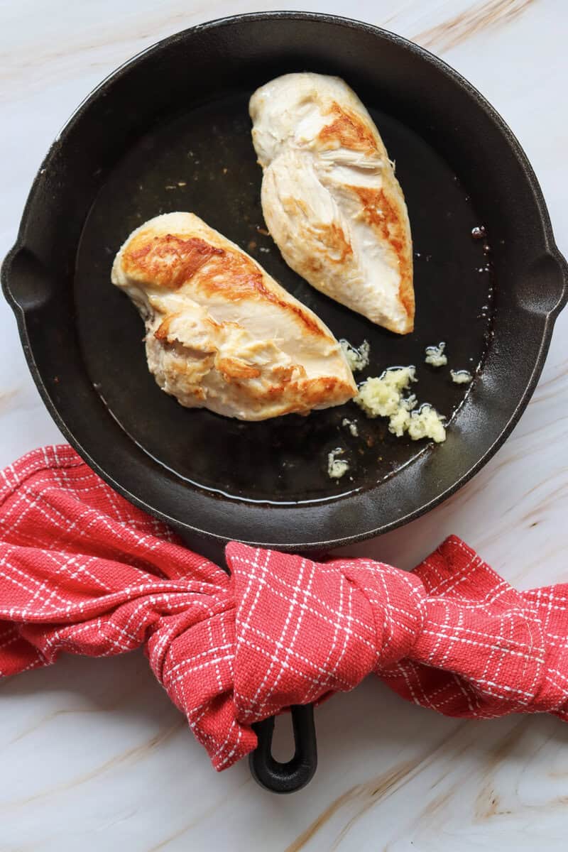 chicken breasts cooking in a cast iron skillet