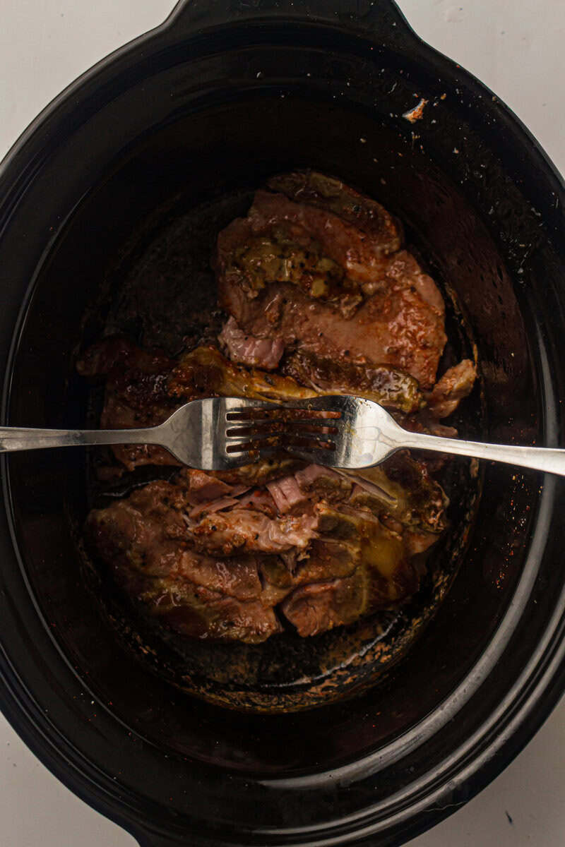 two forks shredding pork in slow cooker