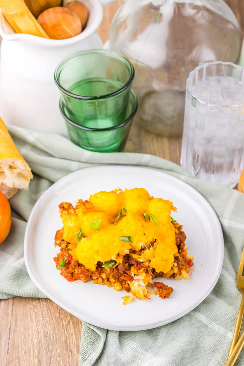 slice of Slow Cooker Chili Cheese Tatertot Casserole  on a plate with a green water glass