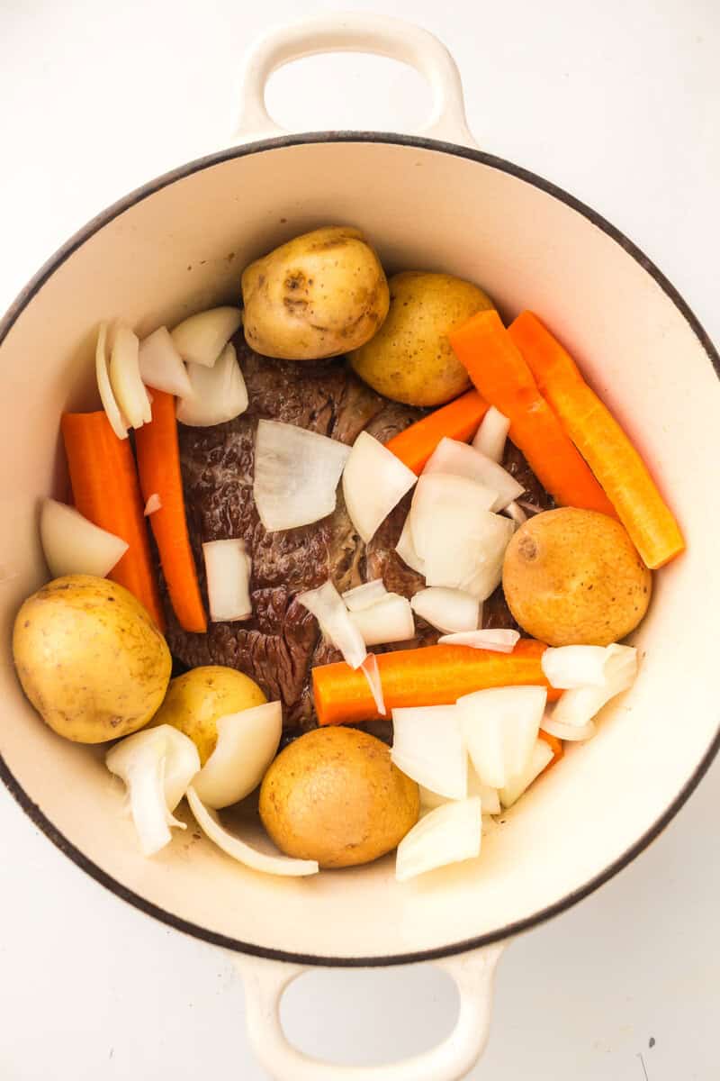 potatoes, carrots, onions and pot roast in a pan