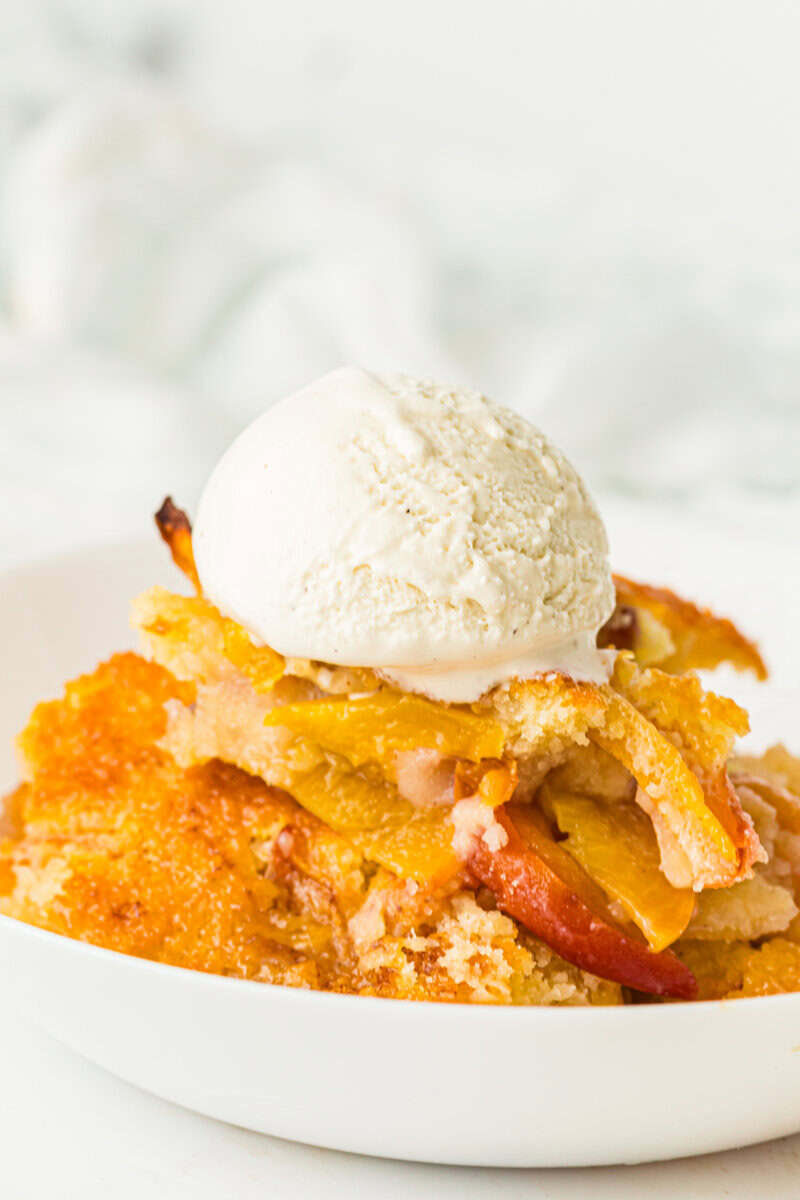 bowl full of peach cobbler with vanilla ice cream