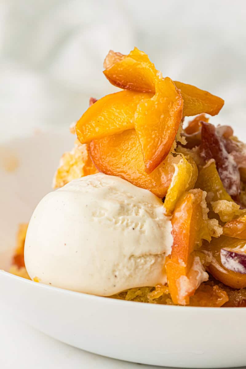 peach cobbler in a bowl with a scoop of vanilla ice cream