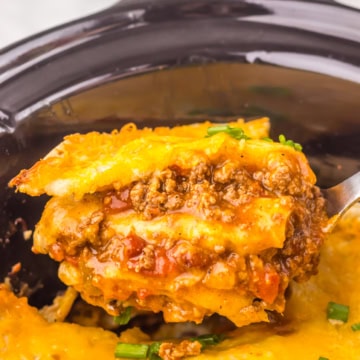 A spoonful of cheesy, layered ground beef casserole being lifted from a slow cooker.