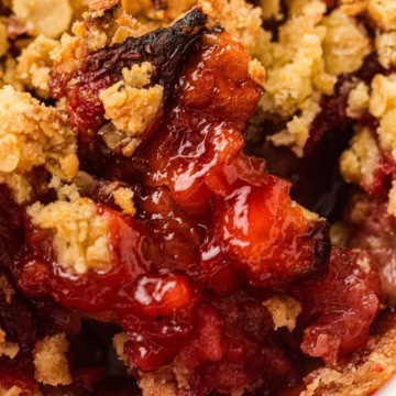 Close-up of a baked strawberry crumble dessert showing juicy red fruit filling and golden brown oat topping.
