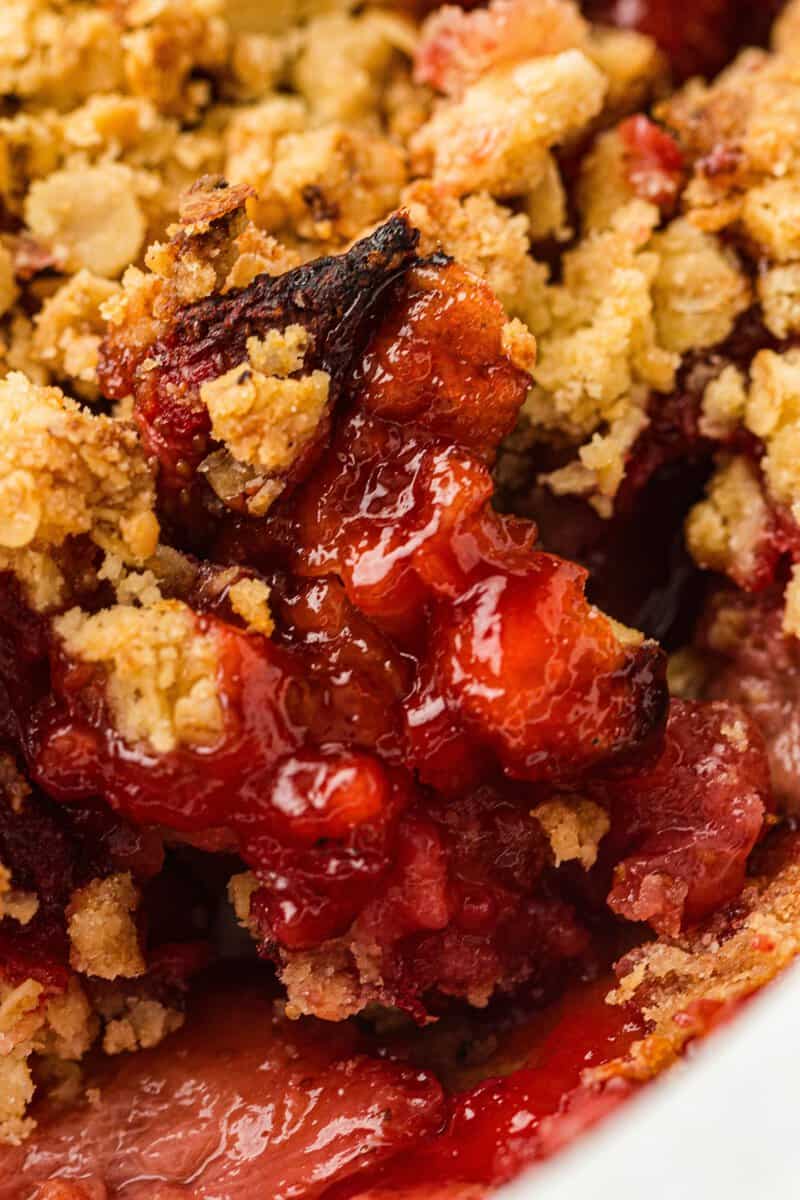 Close-up of a baked strawberry crumble dessert showing juicy red fruit filling and golden brown oat topping.
